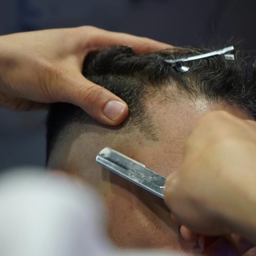 Detailed close-up of a barber using a sharp blade to shave a client's head in a salon.