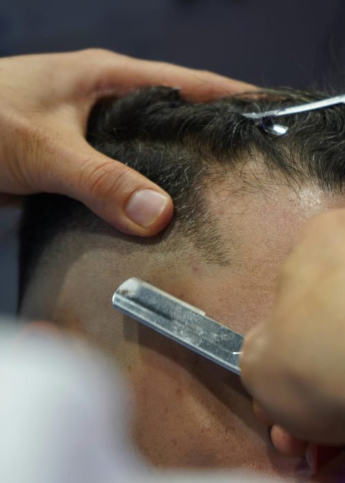 Detailed close-up of a barber using a sharp blade to shave a client's head in a salon.
