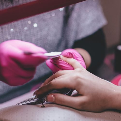 Close-up of a professional manicure session with pink gloves and a nail file in an indoor salon.