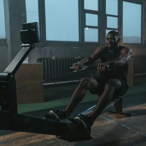 Adult black man intensely working out on a rowing machine indoors. Fitness and strength training concept.