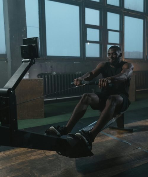 Adult black man intensely working out on a rowing machine indoors. Fitness and strength training concept.