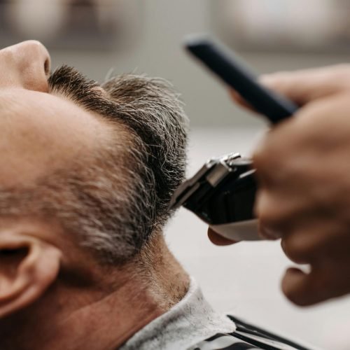 Close-up of a barber using clippers to groom a client's beard in a barbershop.
